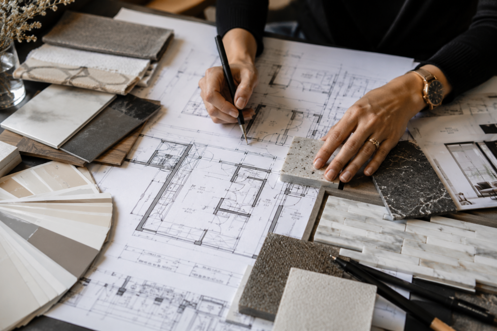 Person reviewing architectural blueprints and examining various tile and material samples, with a fan deck of color swatches nearby on the table.